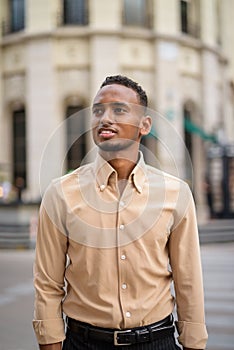 Portrait of happy black young African businessman thinking outdoors in city