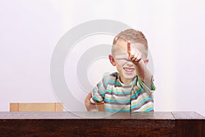 Portrait of happy blond boy child kid pointing at you at the table