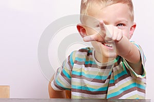 Portrait of happy blond boy child kid pointing at you at the table