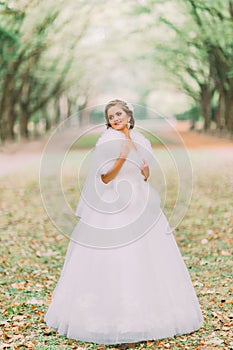 Portrait of happy blonde bride in white dress and fur boa on lane at the autumn park