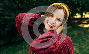Portrait of a happy blonde young woman smiling broadly with a healthy toothy smile, wearing a red sweater, and yellow hat, posing