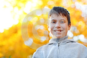 Portrait of happy boy in autumn city park. Posing on trees with yellow leaves. Bright sunlight and golden trees, fall season