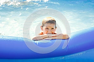 Portrait of a happy boy in a blue pool. A happy child swims in an inflatable pool in the garden on a sunny summer day