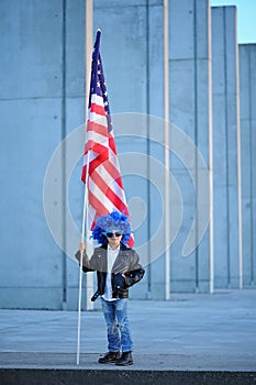 A portrait of happy boy in blue wig holding american flag.