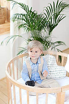 Portrait of a happy boy playing in a baby cot. The boy sits alone in a crib in the nursery. Lonely baby stay in the crib. Waif chi