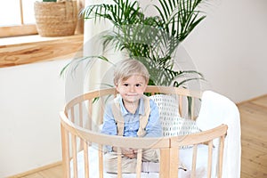 Portrait of a happy boy playing in a baby cot. The boy sits alone in a crib in the nursery. The lonely child stays in the crib. Lo