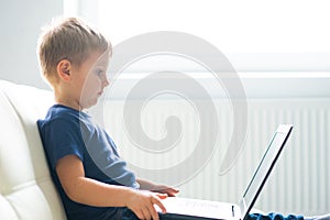 Portrait of happy boy playing with computer. Attractive kid with a laptop at home. Entertainment technology, futuristic