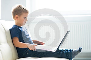 Portrait of happy boy playing with computer. Attractive kid with a laptop at home. Entertainment technology, futuristic