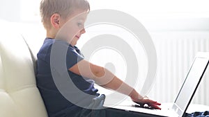 Portrait of happy boy playing with computer. Attractive kid with a laptop at home. Entertainment technology, futuristic