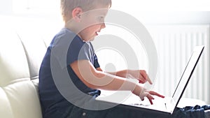 Portrait of happy boy playing with computer. Attractive kid with a laptop at home. Entertainment technology, futuristic