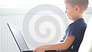 Portrait of happy boy playing with computer. Attractive kid with a laptop at home. Entertainment technology, futuristic