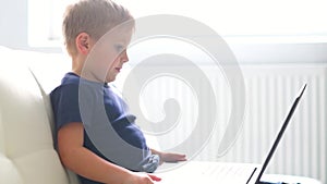 Portrait of happy boy playing with computer. Attractive kid with a laptop at home. Entertainment technology, futuristic