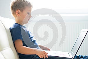 Portrait of happy boy playing with computer. Attractive kid with a laptop at home. Entertainment technology, futuristic