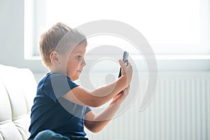 Portrait of happy boy playing with a smartphone. Kid with a mobile phone at home. Entertainment technology, futuristic