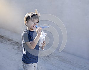 Portrait happy boy playing with toy airplane against blurry wall background, Child throwing foam airplane, Kid playing outside in