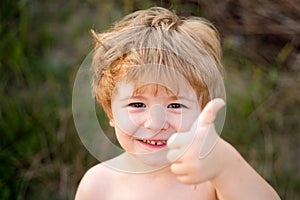 Portrait of happy boy showing thumbs up gesture. Child on nature green background. Summer holidays.