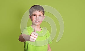 Portrait of happy boy showing thumbs up gesture, isolated over g