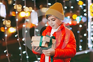 Portrait of a happy boy standing on the evening street and opening a Christmas gift. Christmas gifts, holiday atmosphere