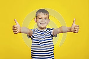 Portrait of happy boy in striped t-shirt showing thumbs up gesture on yellow background