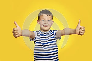 Portrait of happy boy in striped t-shirt showing thumbs up gesture on yellow background