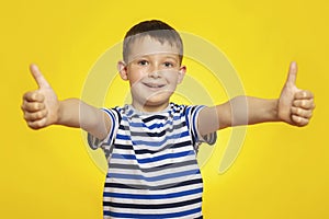 Portrait of happy boy in striped t-shirt showing thumbs up gesture on yellow background