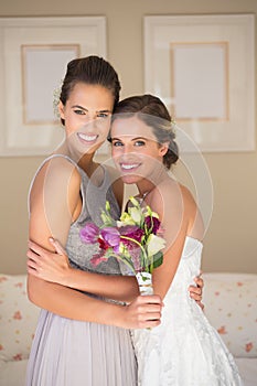 Portrait of happy bride and bridesmaid with bouquet standing in bedroom