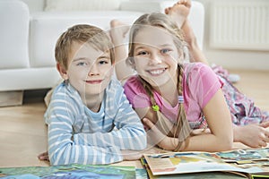 Portrait of happy brother and sister with story books while lying on floor