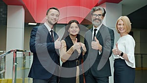 Portrait of happy business people showing thumbs-up hand gesture in office building hall