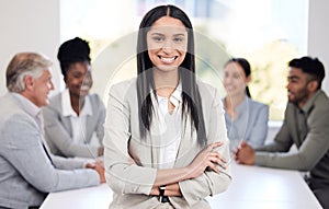 Portrait, happy and a business woman arms crossed in a boardroom with her team planning in the background. Leadership