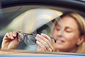 Portrait of a happy business woman holding eyeglasses and smiling at camera while sitting behind steering wheel of her