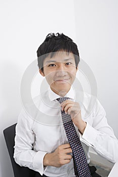 Portrait of happy businessman adjusting necktie at office