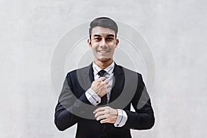 Portrait of Happy Businessman in Black Formal Suit. Standing by the Cement Wall, Touching Neck Ties