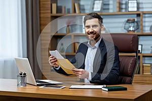 Portrait of happy businessman investor, mature adult man smiling and looking at camera, boss holding message envelope