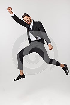 Portrait of a happy businessman jumping in air against isolated white background.