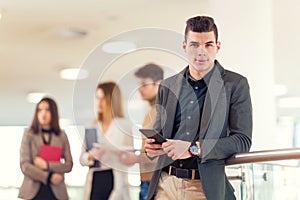 Portrait of happy businessman in office holding digital tablet.