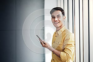 Portrait of Happy Businessman Standing by the Window in Office. Using Smartphone and Smiling