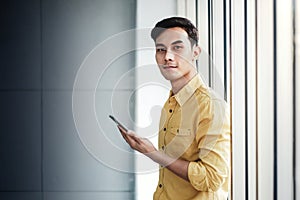 Portrait of Happy Businessman Standing by the Window in Office. Using Smartphone and Smiling