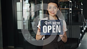 Portrait of happy businesswoman in apron holding open sign standing in new cafe