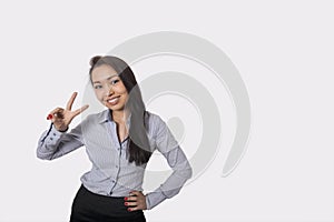 Portrait of happy businesswoman showing victory sign against gray background