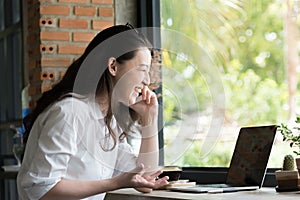 Portrait of a happy businesswoman sitting and use internet smartphone with laptop computer at her workplace office
