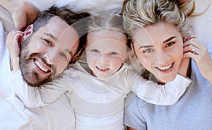 Portrait of happy carefree caucasian family in pyjamas from above lying cosy together in bed at home. Loving parents