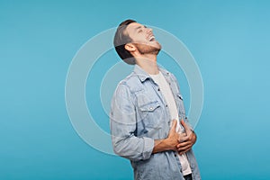 Portrait of happy carefree man in worker denim shirt laughing out loud and holding belly, chuckling