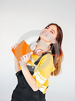 Portrait of happy carefree smiling teenager girl with dark long hair in yellow t-shirt with copybook on grey background