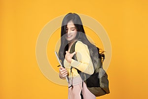 Portrait of happy casual Asian girl student with backpack and laptop  on yellow background. Back to school and learning