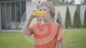 Portrait of happy Caucasian boy drinking yellow refreshing juice and smiling at camera. Cheerful kid with healthful