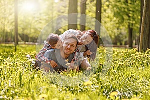 Portrait of happy Caucasian family lying in hugs on green grass in park on sunny summer day.