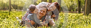 Portrait of happy Caucasian family lying in hugs on green grass in park on sunny summer day.