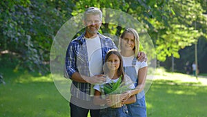 Portrait of the happy caucasian family standing in the park, the girl holding the pot with the plant before planting