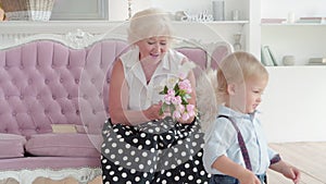 Portrait of happy Caucasian grandmother receiving flowers from grandson and talking. Positive senior woman meeting cute