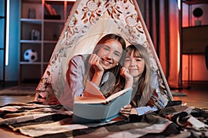Portrait of happy caucasian loving sisters smiling and looking at camera inside wigwam.